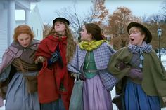 four young women dressed in period clothing standing outside on the snow covered ground with their mouths open