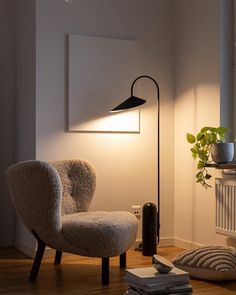 a living room with a chair, lamp and books on the floor