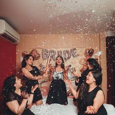 a group of women sitting on top of a bed with confetti in the air