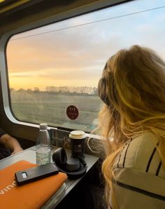 two people sitting on a train looking out the window at an open field with trees