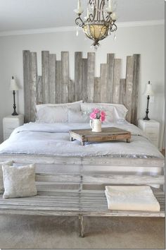 a white bed with wooden headboard and chandelier hanging from it's ceiling