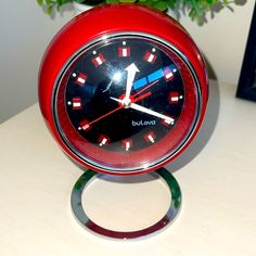 a red clock sitting on top of a table next to a vase filled with flowers