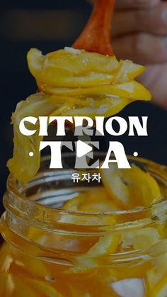 a jar filled with sliced lemons and sitting on top of a table next to a hand holding a spoon