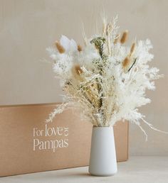 a white vase filled with dried flowers next to a cardboard box that says to love pampas