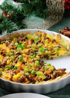 a casserole with meat, cheese and green onions in a white dish on a table