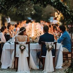 a group of people sitting at a table with white cloths and flowers in front of them