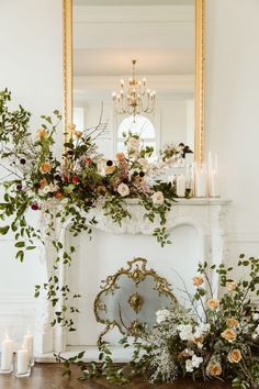 a fireplace with flowers and candles on it in front of a mirror that is above the mantle