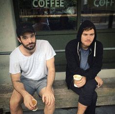 two men sitting on a bench with coffee in their hands