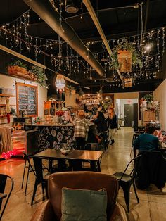 people sitting at tables in a restaurant with lights hanging from the ceiling and potted plants on the walls