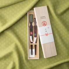 This set, named uchiiwai after the Japanese custom of giving return or thank you gifts, includes two pairs of dark brown-lacquered wood chopsticks with glittering tops. They offer the classy sheen of traditional lacquerware coupled with an eye-catching design. The longer pair measures 22.5 cm (8.8 in) and is accented with green and silver detailing, while the shorter pair is 20.5 cm (8.1 in) in pink and silver. The chopsticks are presented in a paulownia wooden box, adorned with a Japanese noshi Glitter Top, Green And Silver, Japanese Characters, Lacquered Wood, Pink And Silver, Traditional Crafts, Chopsticks, Chopsticks Set, Wood Boxes