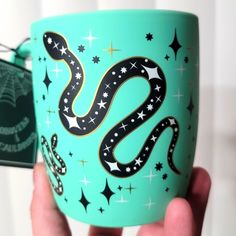 a hand holding a green coffee cup with a black and white snake on it