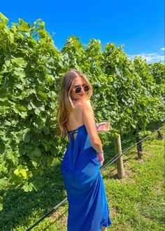 a woman in a blue dress standing next to a vineyard