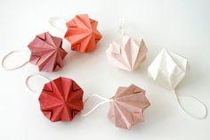 three origami flowers are tied to strings on a white surface, one is pink and the other is red