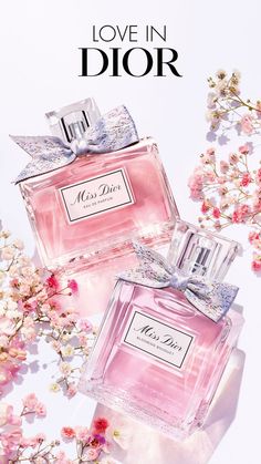 two pink perfume bottles sitting next to each other on top of a white surface with flowers