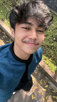 a young man with a moustache on his face posing for a photo in the park