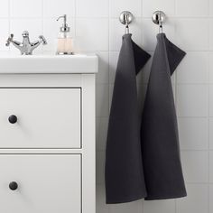 two black towels hanging on the wall next to a white cabinet and sink with faucet