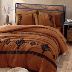 an orange comforter set with black trimmings in a bed room next to a wooden floor