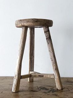 an old wooden stool sitting on top of a wooden floor next to a white wall