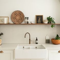 a kitchen with white cabinets and open shelving above the sink is filled with potted plants