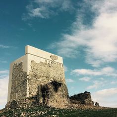 an old stone tower sitting on top of a lush green hillside under a blue sky