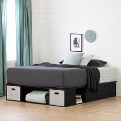 a bed with two storage bins underneath it in a room next to a window