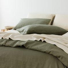 an unmade bed with green sheets and pillows