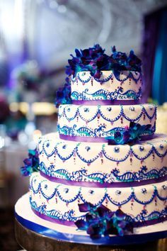 a three tiered cake with purple and blue decorations on the top is sitting on a table