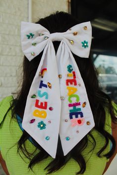 the back of a woman's head wearing a white bow with colorful letters on it