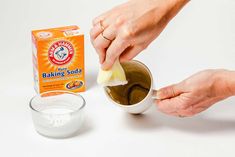 two hands holding a sponge over a bowl with baking soda next to it and a carton of baking soda