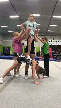 a group of people standing on top of each other in a gym with one person upside down