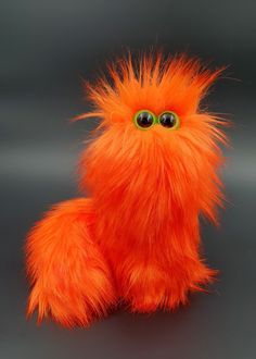 an orange furry toy with green eyes sitting on a table next to a gray background