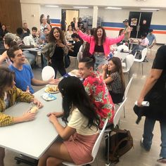 a group of people sitting around a table eating food and talking to each other in a room