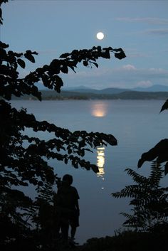 two people are standing by the water looking at the moon