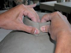 two hands are working on a clay vase