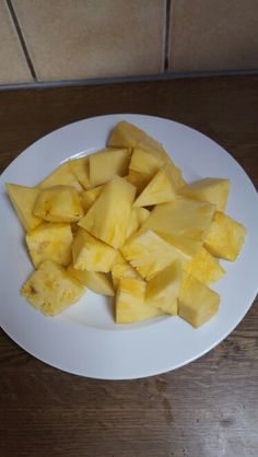 cut up pieces of pineapple on a white plate sitting on a wooden table top