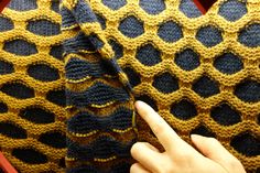 a hand pointing at the edge of a crocheted blanket that is yellow and blue