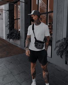 a man with tattoos and suspenders is standing on the sidewalk in front of a building