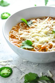 a white bowl filled with soup and garnished with cilantro, green peppers and parsley