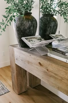 two vases with green plants on top of a wooden table next to a mirror