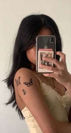 a woman taking a selfie with her cell phone and butterfly tattoos on her arm