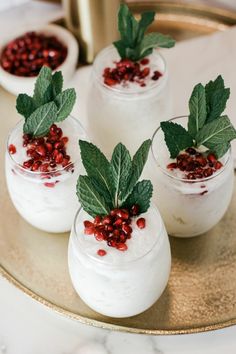 three glasses filled with pudding and topped with green leaves on a gold platter next to other desserts