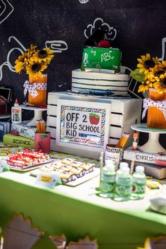 a table topped with lots of cakes and desserts next to a chalkboard wall