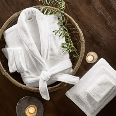 white towels tied up in a basket next to candles and some greenery on a wooden table