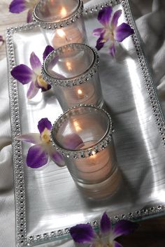 three glass vases with flowers in them on a silver tablecloth covered table cloth