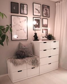 a white dresser sitting next to a window with pictures on the wall above it and a plant