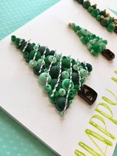 some green buttons are hanging on a white card with black and silver pins in the shape of a christmas tree