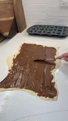 a person is spreading chocolate frosting on top of an uncooked cookie sheet