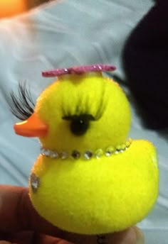 a small yellow toy duck with eyelashes on it's head is being held by someone