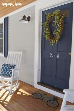 two white rocking chairs sitting on a porch next to a blue front door with a wreath