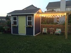 a small shed with lights on the roof and chairs in front of it, next to a fence